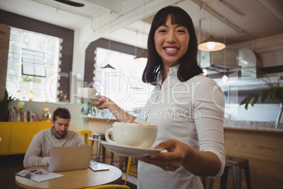 Portrait of waitress holding coffee cups with man using laptop at table