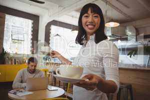 Portrait of waitress holding coffee cups with man using laptop at table