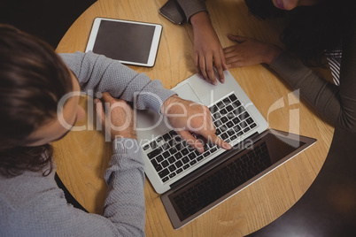 Man with friend pointing at laptop in cafe