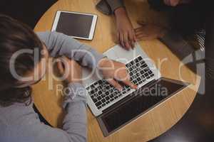 Man with friend pointing at laptop in cafe