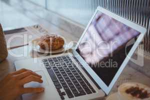 Cropped hand of woman using laptop in cafe