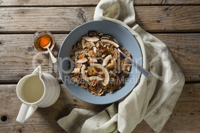 Bowl of breakfast cereal, honey and milk on wooden table