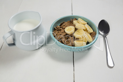 Wheat flakes and banana slice in bowl with milk jug