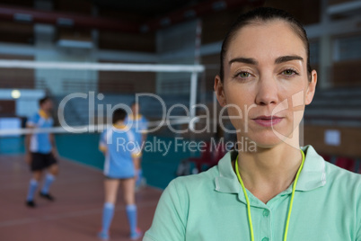 Portrait of confident coach with volleyball players in background