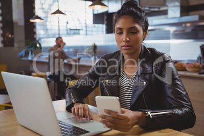 Woman with laptop using phone in cafe