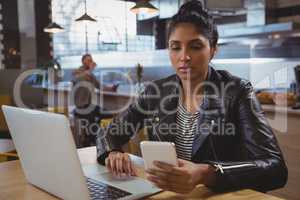 Woman with laptop using phone in cafe