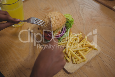 Cropped hands of man having burger and French fries in cafe