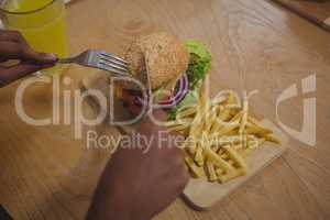 Cropped hands of man having burger and French fries in cafe