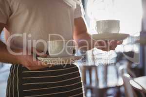 Mid section of waiter holding coffee cups in cafe