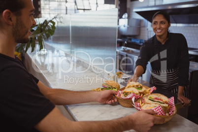 Smiling waitress giving baskets with food to coworker in cafe