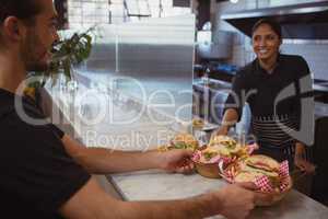 Smiling waitress giving baskets with food to coworker in cafe