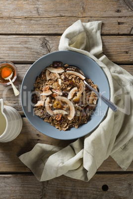 Bowl of breakfast cereal, honey and milk on wooden table