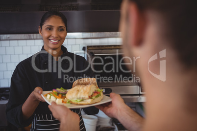 Smiling waitress giving plate with food to coworker