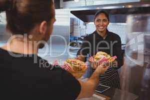 Smiling waitress giving baskets with food to coworker