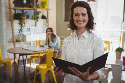 Portrait of confident waitress with menu in cafe