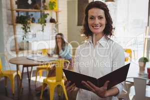 Portrait of confident waitress with menu in cafe