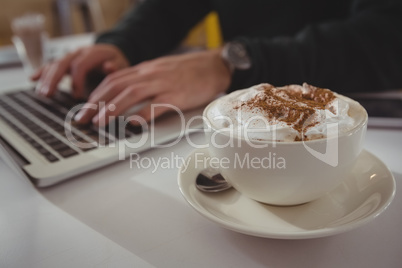 Cropped hands of businessman using laptop by coffee cup