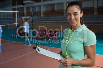 Portrait of smiling coach holding clipboard at volleyball court