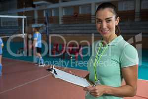 Portrait of smiling coach holding clipboard at volleyball court