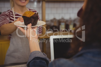 Mid section of owner serving muffin to customer