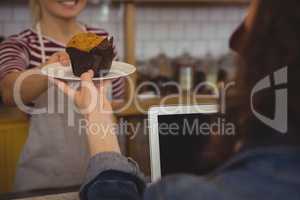 Mid section of owner serving muffin to customer