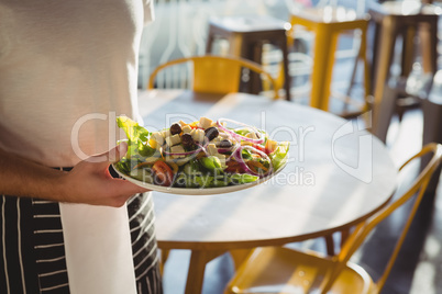 Mid section of waiter holding plate with salad