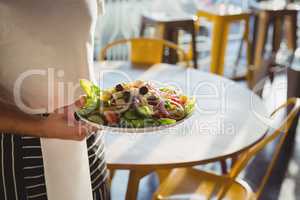 Mid section of waiter holding plate with salad