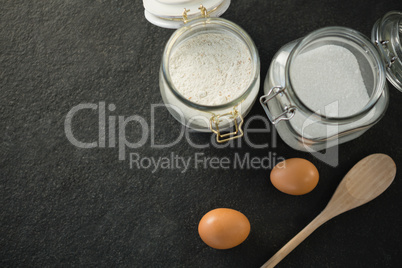 Directly above shot of wooden spoon by eggs with sugar and flour in  jar