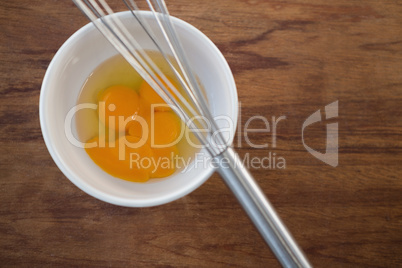 Overhead view of egg in bowl with wire whisk
