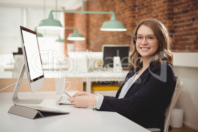 Portrait of smiling female executive using mobile phone while working on computer