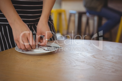 Mid section of waitress arranging plate on table