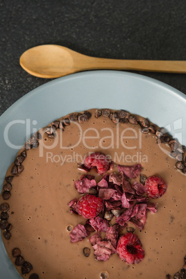 Chocolate syrup with fruits in bowl on black background