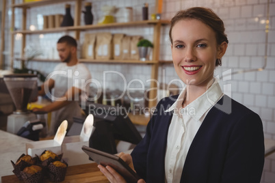 Portrait of smiling owner using tablet with waiter working in cafe