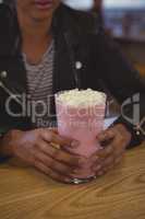 Mid section of woman with milkshake glass in cafe