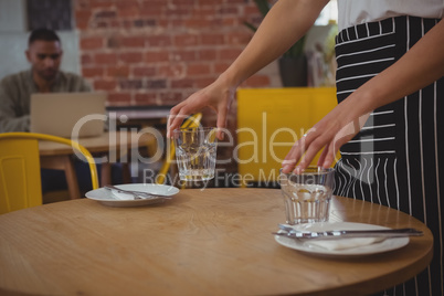Mid section of waitress arranging glasses on table