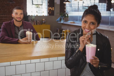 Portrait of woman with friend enjoying milkshake in cafe