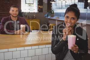 Portrait of woman with friend enjoying milkshake in cafe