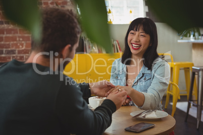 Man putting ring on woman finger at cafe