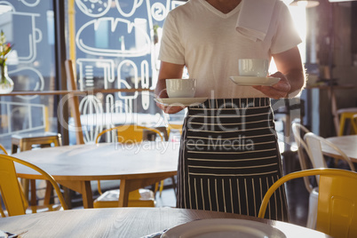 Mid section of waiter holding coffee cups