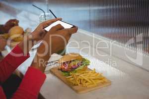 Cropped hands of woman photographing French fries in cafe
