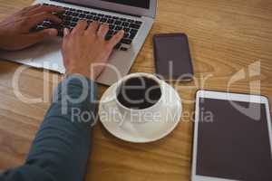 Cropped hands of man with coffee using laptop in cafe