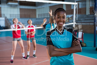 Smiling female volleyball player standing with arms crossed in the court