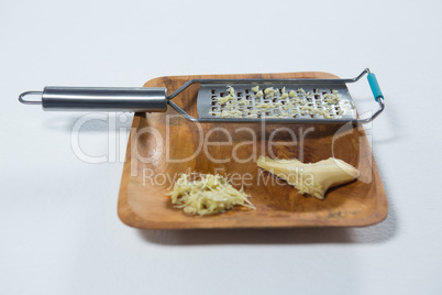 Close up of steel grater and fresh ginger on wooden plate