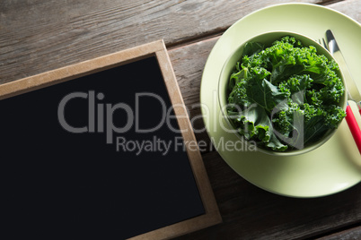 High angle view of kale in bowl on plate by blackboard