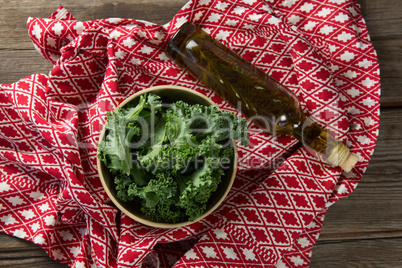 Fresh kale in bowl with oil bottle and fabric on table
