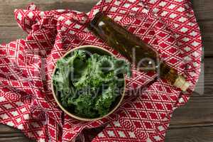 Fresh kale in bowl with oil bottle and fabric on table