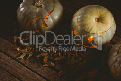 Illuminated white jack o lanterns with autumn leaves on table