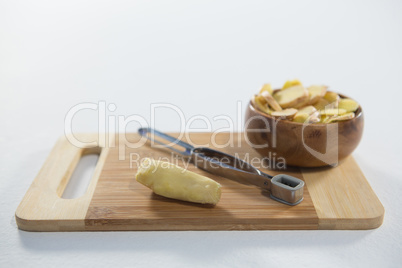 High angle view of peeler and fresh ginger with bowl on wooden cutting board