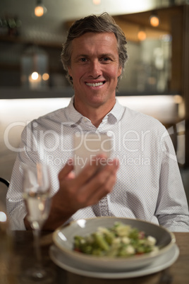 Happy man using mobile phone while dining in restaurant