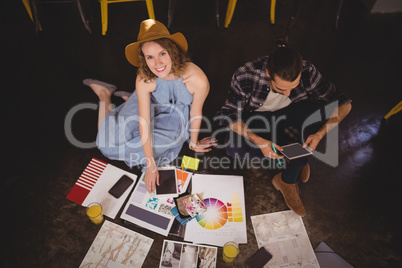 High angle portrait of smiling young female designer sitting by male colleague with sheets